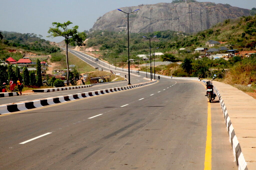 The road south out of Ado-Ekiti, empty, curving past the rock under a haze sky.
